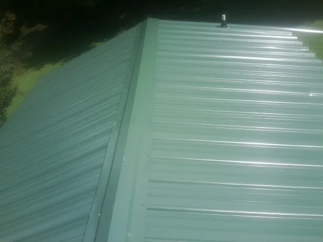 New green metal panels meeting at the ridge of a roof — Flat Roof Repair work by our crew in Northwood